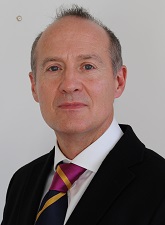 Head and shoulders photo of Andy Callaghan. Andy is wearing a dark jacket, white shirt and a purple and blue tie.