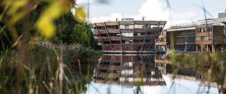 Photo of the Djanogly Learning Resource Centre on Jubilee Campus. Campus buildings and the walkway can be seen on the left on the photo and the lake and trees are on the right.