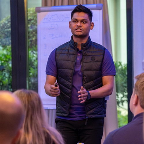 Kaustubh Nande wearing a black gilet, standing in front of a large pad on a stand, presenting to people sitting down facing him
