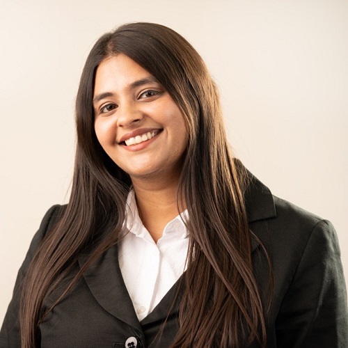 Photo of Mahima Udani. Mahima is smiling, has long hair and is wearing a black jacket and white shirt.