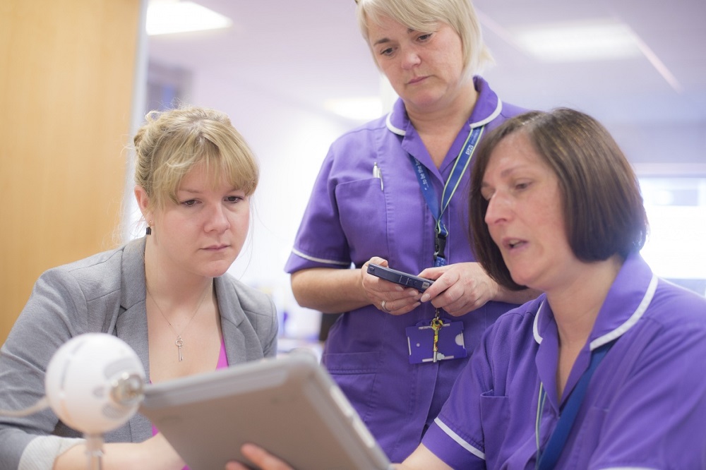 3 female healthcare professionals in uniform looking at a electronic tablet