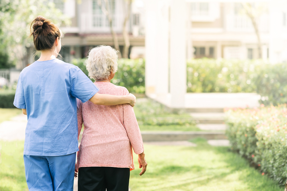 A care worker with her arm around an elderly woman giving her support whilst walking in the garden of a care home.