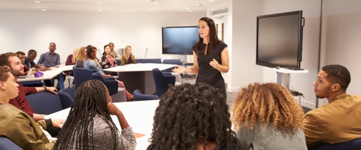 A female teacher addressing university students in a classroom