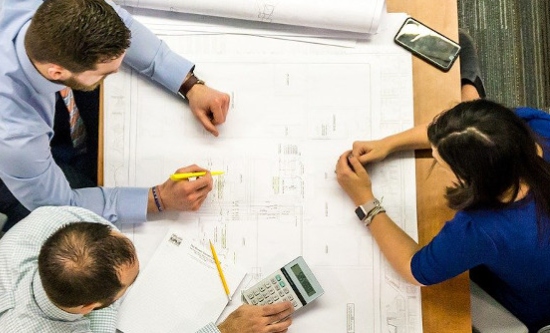 Three people looking at an architectural drawing on a table