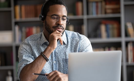 Man wearing headphones looking at laptop, thoughtful