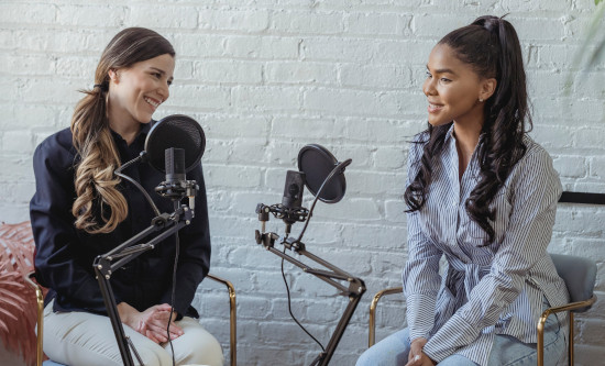 Two women sitting in front of microphones recording podcast