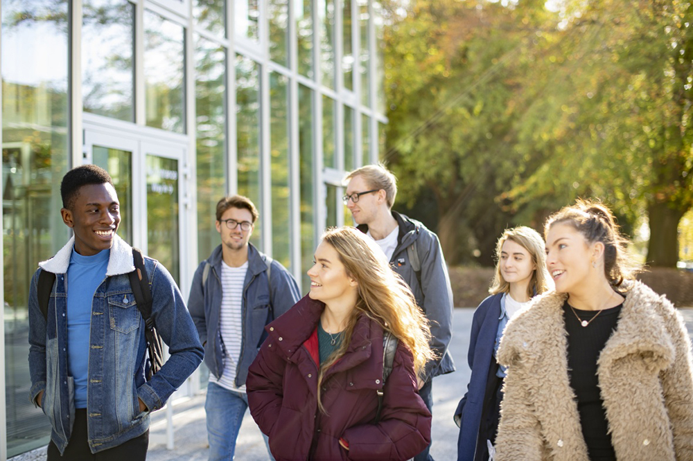 A group of students walk outside the Monica Partridge building smiling and chatting