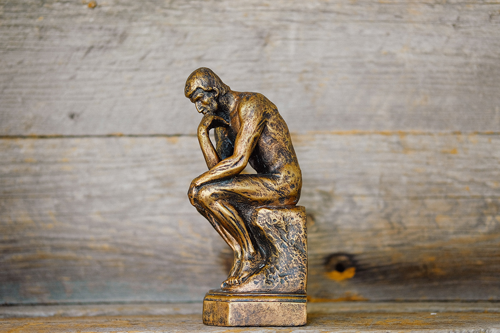 A small brass figurine sits in a stereotypical thinking pose against a wooden background