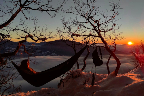 A person lying down in a hammock on top of a snowy mountain.