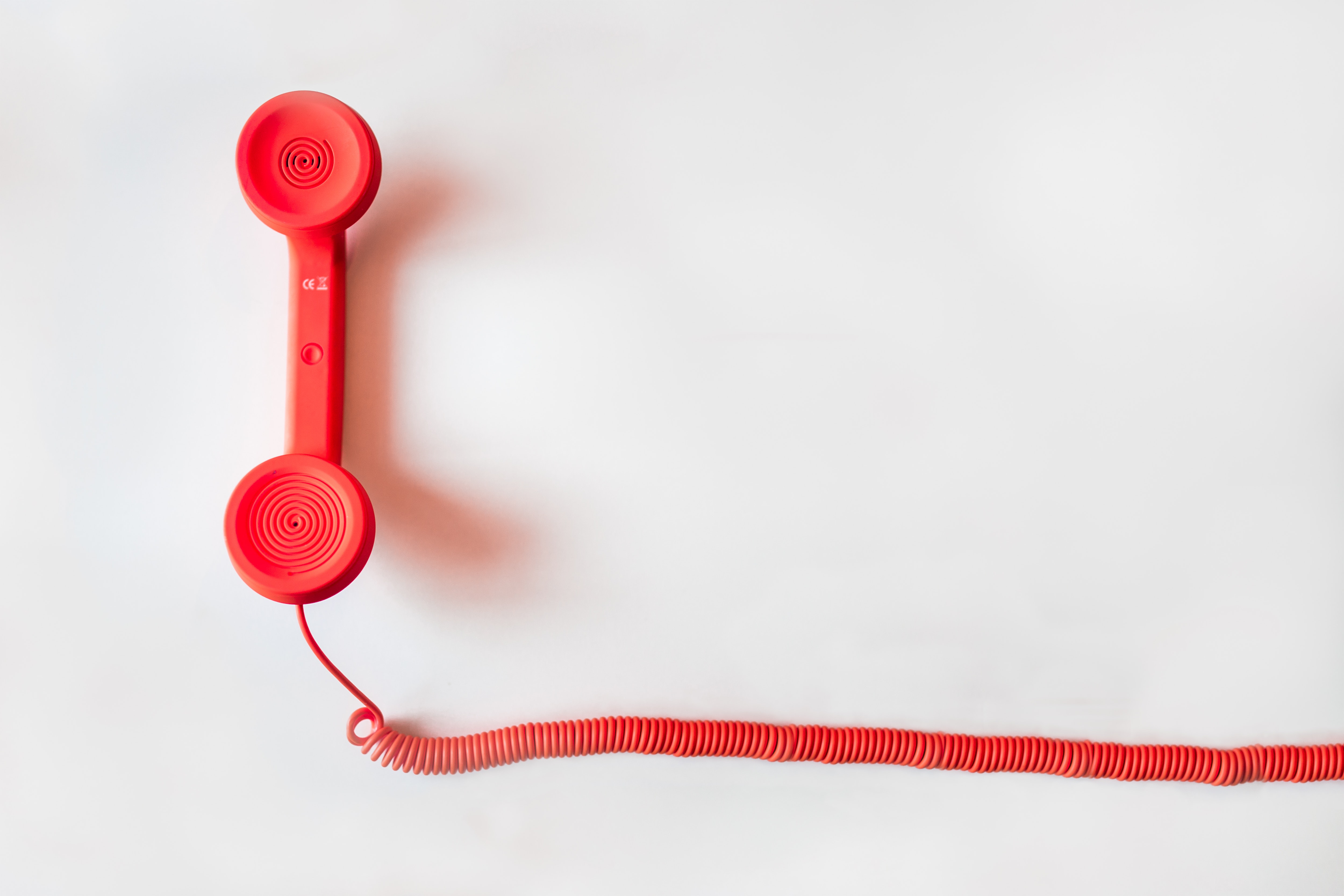 Red old style telephone handset with length of red spiral cord coming from bottom of the handset