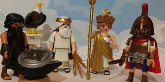 Photo of four Playmobil toy figures dressed as ancient gods with an eagle on a plinth beside them.