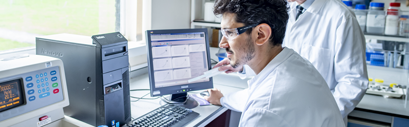 Researcher in a lab coat looking at a computer screen and smiling