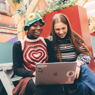 Two students looking at a laptop and laughing