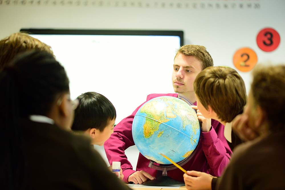 Male geography in classroom with pupils looking at a globe