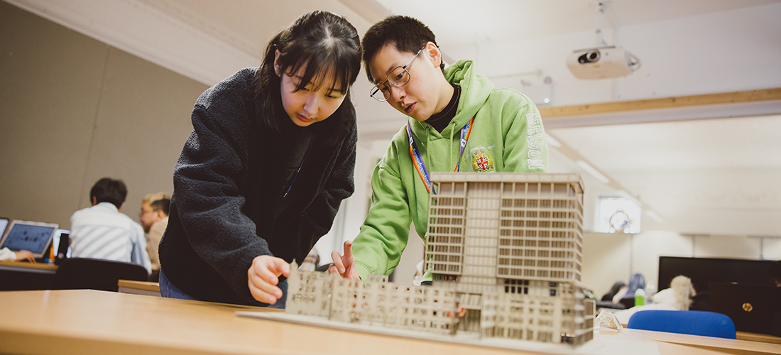 Two students in a classroom looking at an architectural model of a building complex