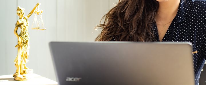 Gold statue of lady justice on a table next to a woman looking at a laptop