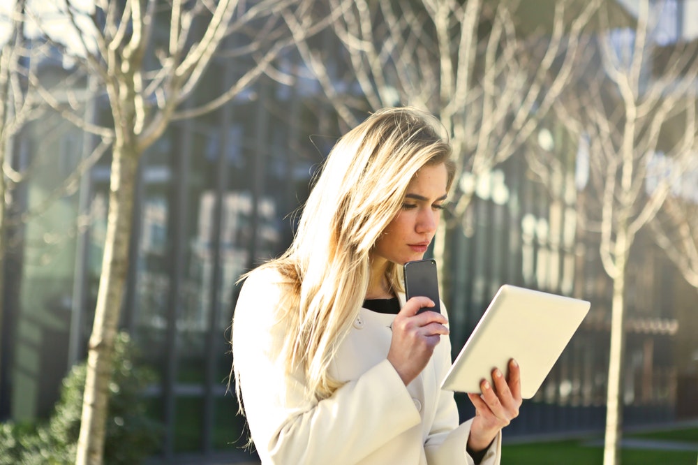 Brown haired woman holding a white wireless device outdoors