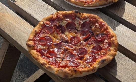 Picture of a pizza on a wooden bench outdoors