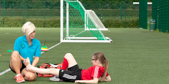 A female student on placement, examining a client's ankle on a football pitch.