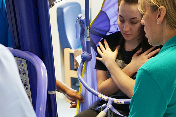 a woman being hoisted in a sling by health professionals