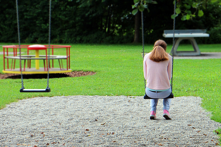 A young woman sitting on a swing in a playground looking lonely.