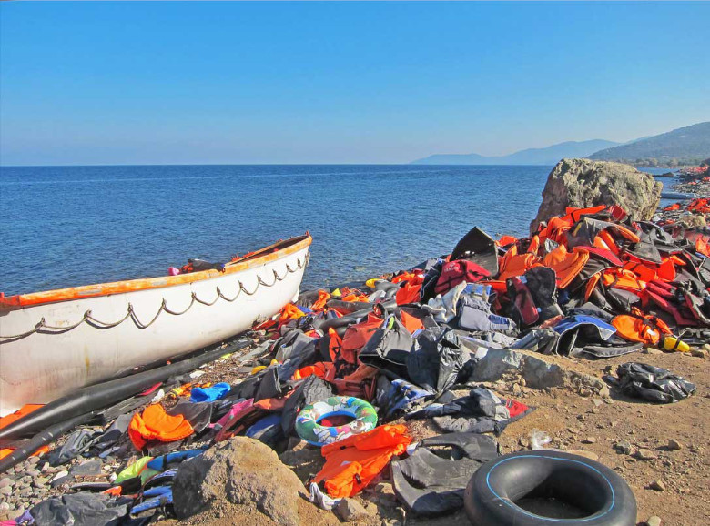 Refugee boat on a beach with lots of discarded life jackets.