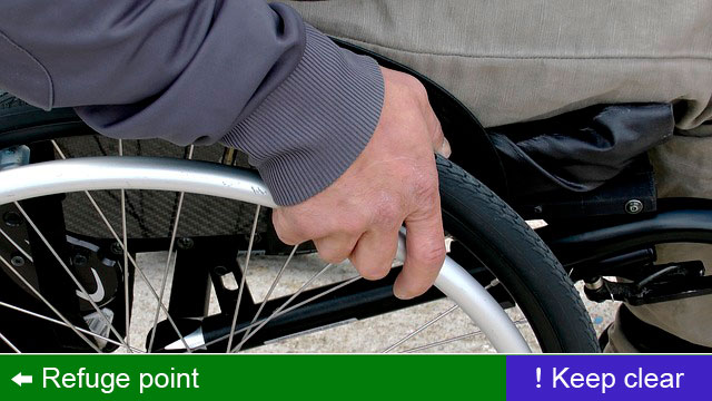 Man in wheelchair with refuge point and keep clear signage