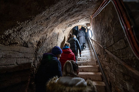 Visitors climbing steep steps through a sandstone tunnel.