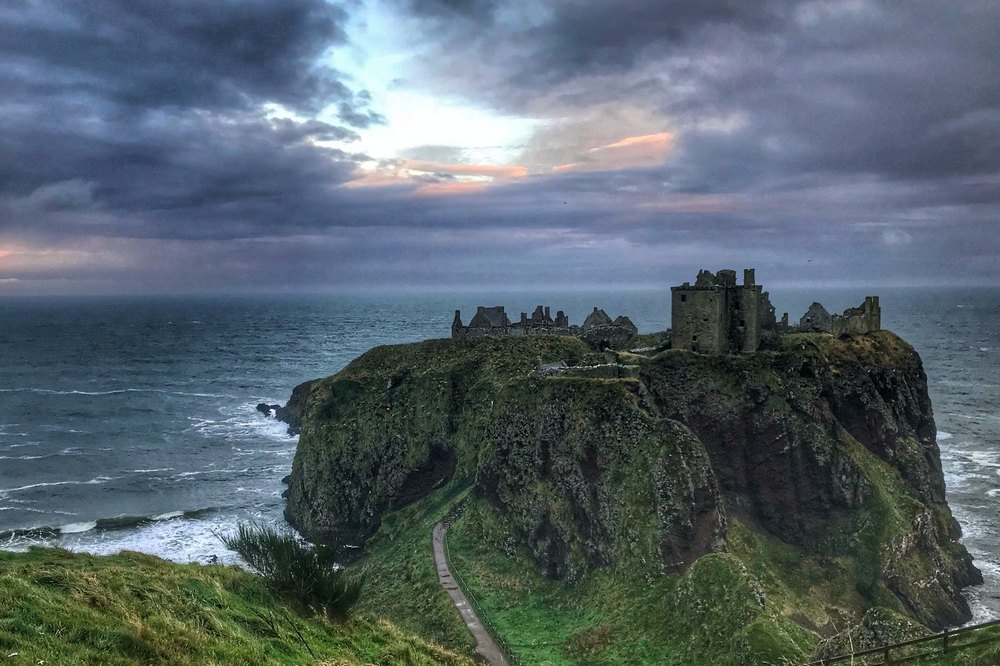 Castle ruins on an outcrop of rock with a stormy ocean in the background