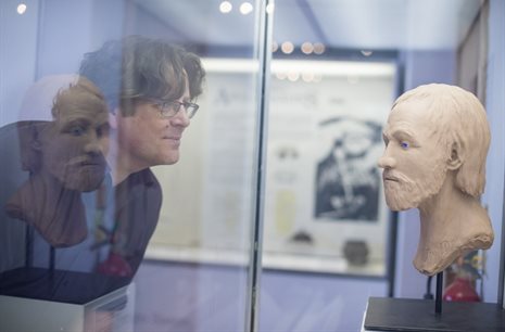A person in a museum looking at a bust in a glass case.