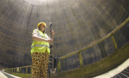 Bass clarinet-ist dressed in hi-vis safety gear playing in abandoned power station cooling tower