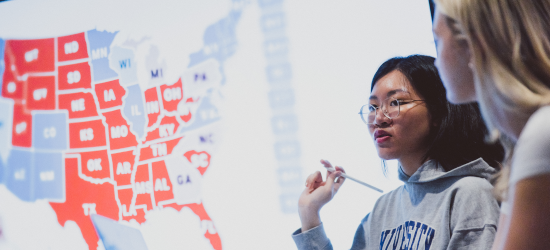 Two students in seminar room with map of the United States of America behind them