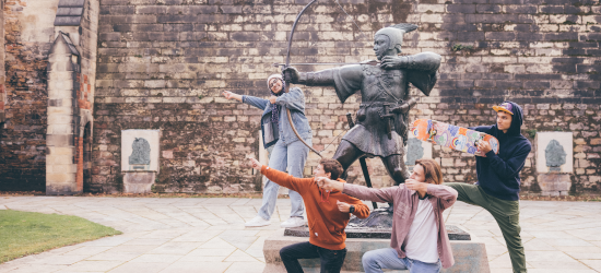 Statue of Robin Hood firing arrow surrounded by mixed group of students copying pose