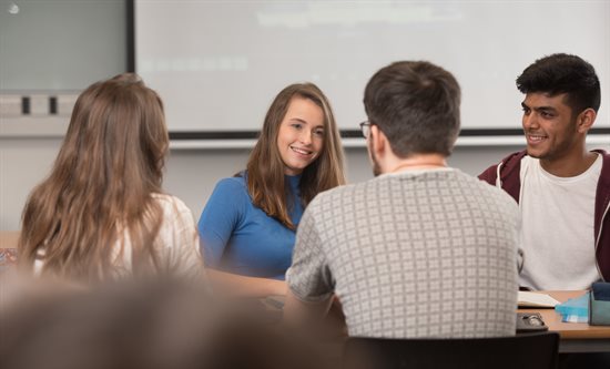 Group of students sitting around a table talking and smiling