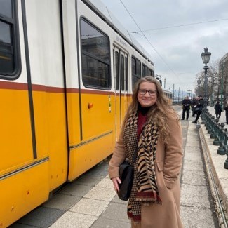 Paige stands in front of a tram and smiles at the camera