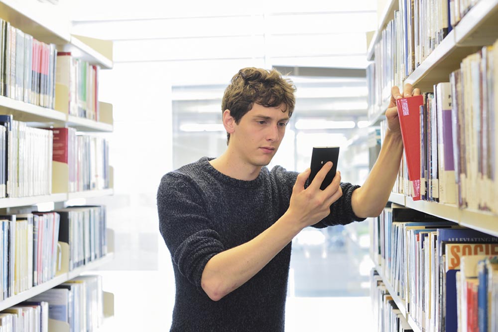Student using a mobile phone in the book shelves