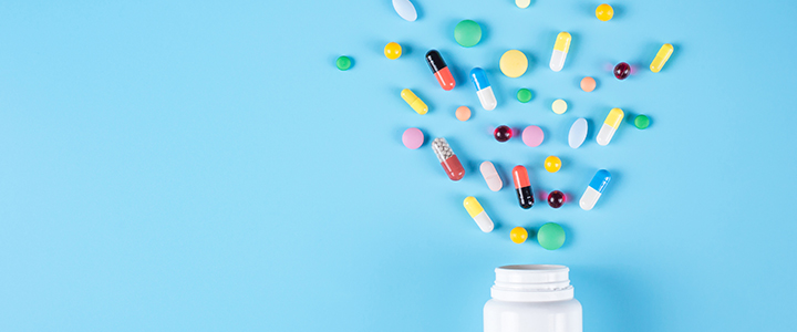 Medical tablets, capsules and caplets flying out of a bottle against a light blue background