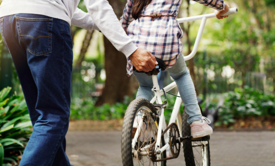 A parent supporting a child riding a bicycle in a park.