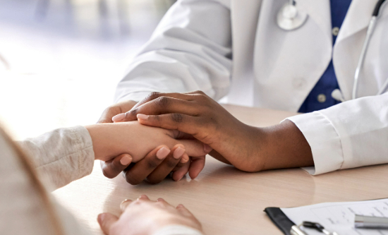 A doctor's hands clasping a patient's hand across a table.