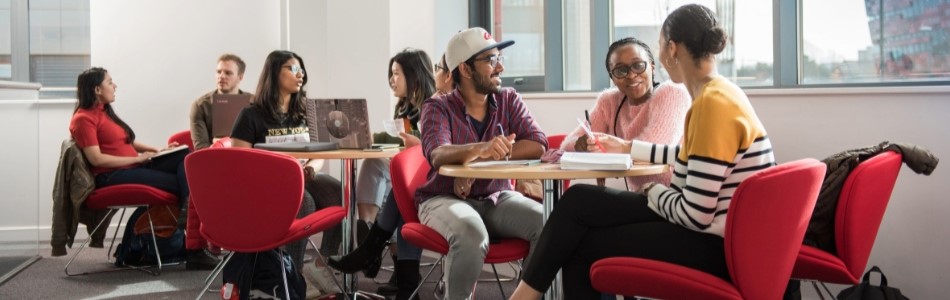 Eight postgraduate students sitting at three small round tables, talking and studying.