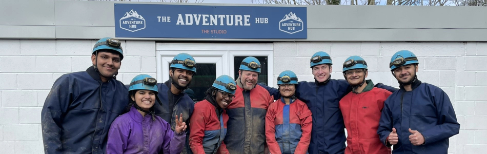 Sports and exercise medicine students and staff wearing caving gear in front of a building called "The Adventure Hub".