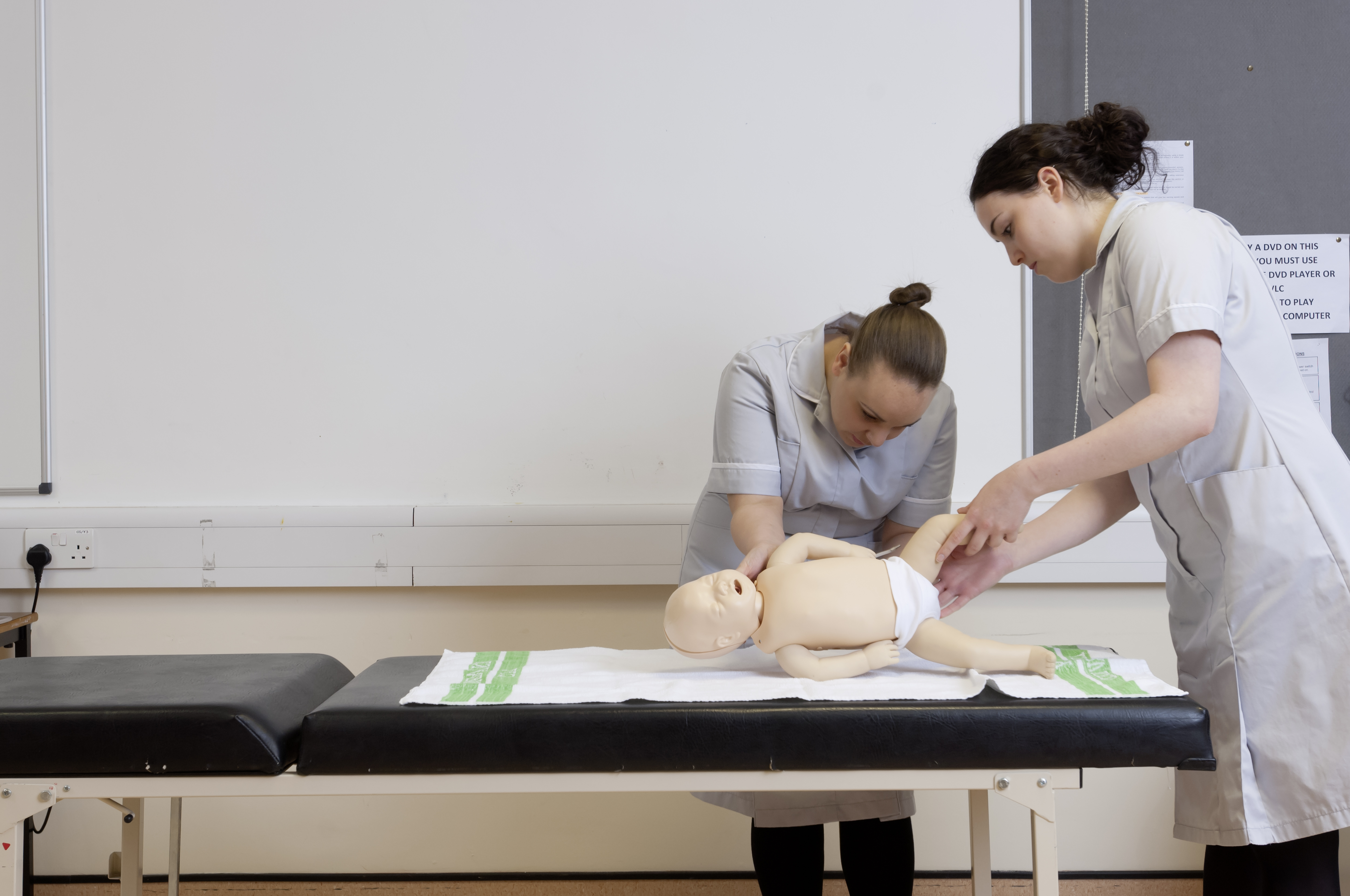 two Midwifery students practicing on a prosthetic baby