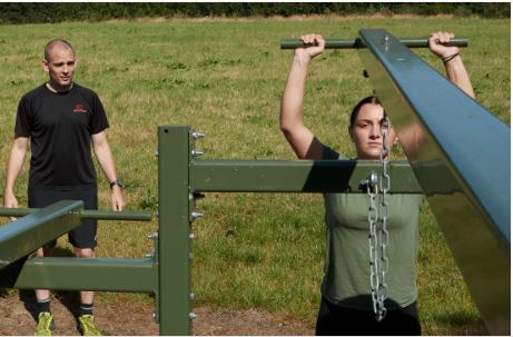 Two women using apparatus to exercise on with coach standing by