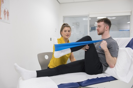 Physiotherapy student guiding a patient through leg exercises with a giant band