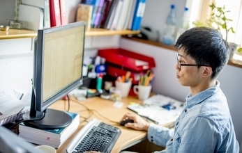 A male student studying at a desktop PC in his office