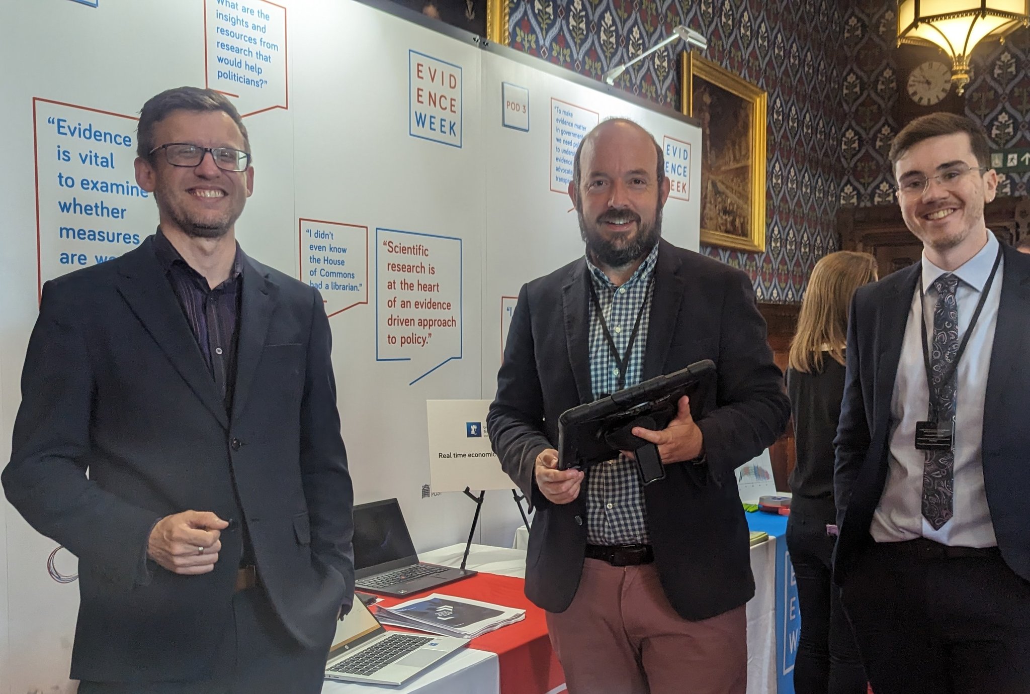 Chris, Max and John smile in front of Evidence Week 2023 display
