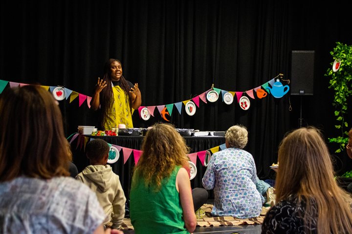 Black woman in apron talks to audience of women and children