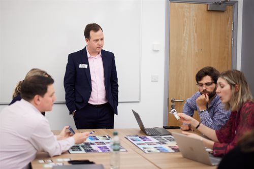 A white man standing across table with a group of people