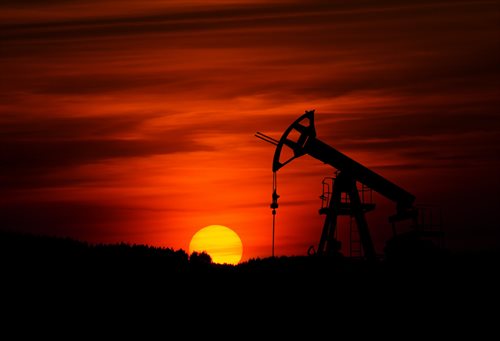 Pump-jack mining crude oil silhouetted against an angry red sunset
