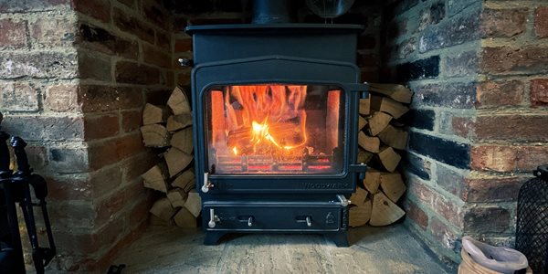 Lit wood burning stove surrounded by logs